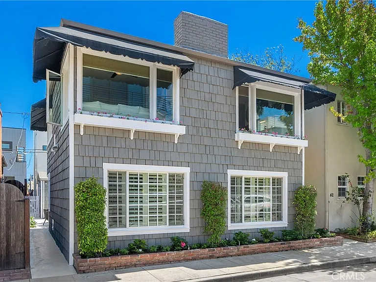 Two-story gray house with large windows, black awnings, and white shutters